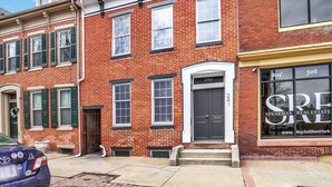 A red brick building with a black door, a window with a 'Buy Sell Rent' sign, and a car parked in front. - NEW Downtown York 2B Getaway. Modern Comfort. (York)