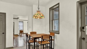 A dining area with a wooden table and chairs, a hanging light fixture, and a window with blinds. - NEW Downtown York 2B Getaway. Modern Comfort. (York)