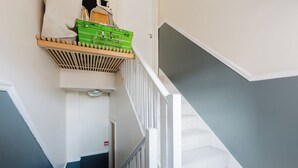 Un escalier avec une rampe, un panier fixé au mur et une porte avec un panneau rouge indiquant la sortie de secours.