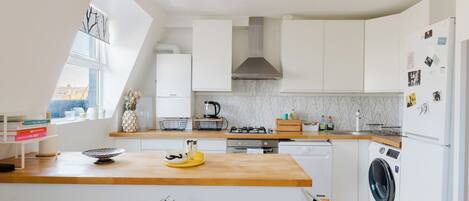 A modern kitchen with white cabinetry, a wooden countertop, a gas stove, a built-in oven, a washing machine, and a window providing natural light.