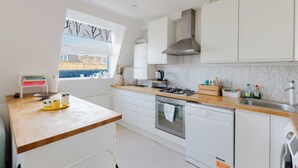 Une cuisine moderne avec des meubles blancs, un plan de travail en bois, une cuisinière à gaz, un four et un lave-vaisselle.