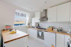 A modern kitchen with white cabinets, a wooden countertop, a gas stove, an oven, and a dishwasher. - Sunny 1BD Flat in the Heart of Maida Vale (Greater London)