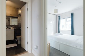 A hotel room with a bed, a window with curtains, a bedside table, and a small stool. - Sunny 1BD Flat in the Heart of Maida Vale (Greater London)