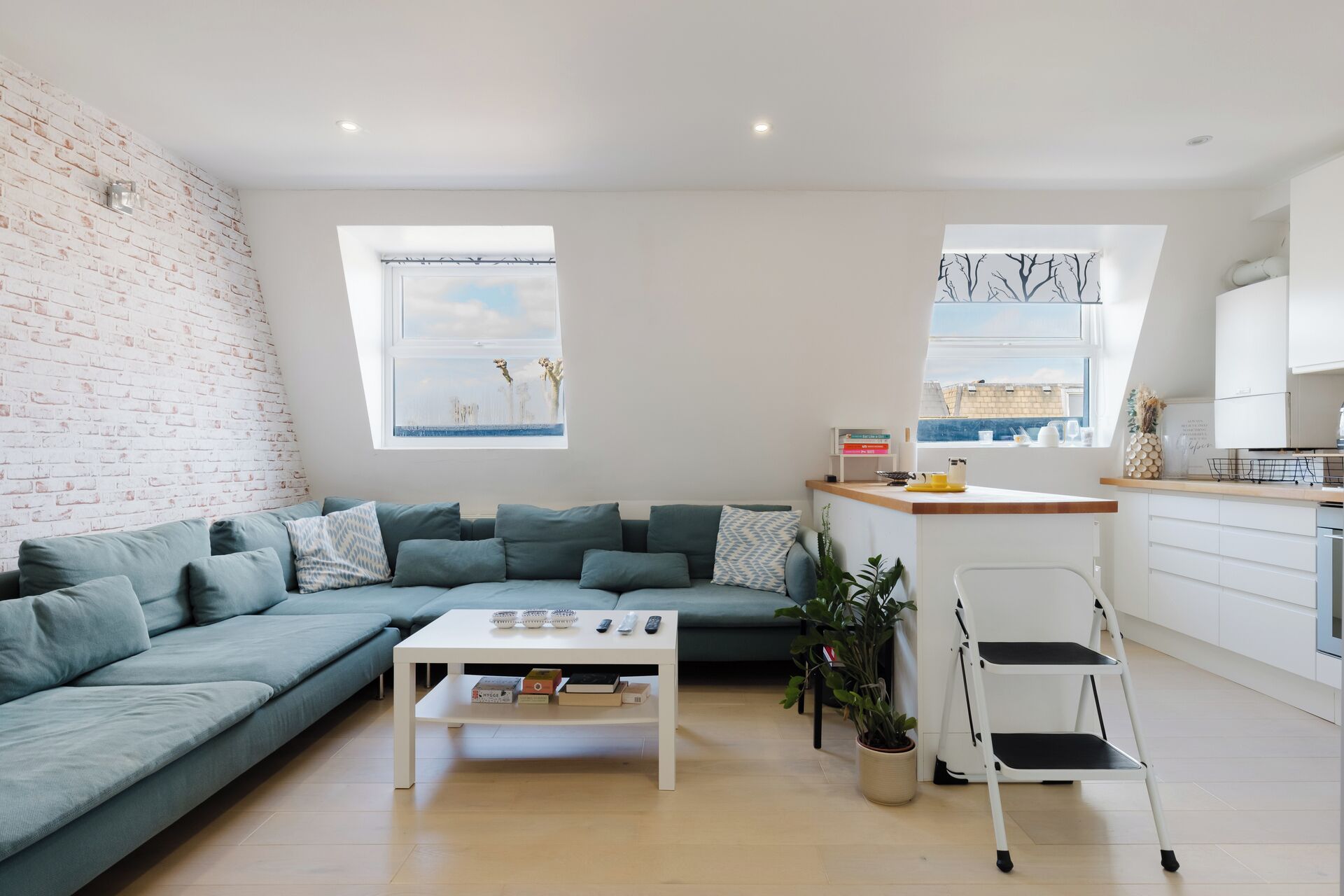 A modern living room with a sectional sofa, a white coffee table, and a kitchen area with a white countertop and cabinets.