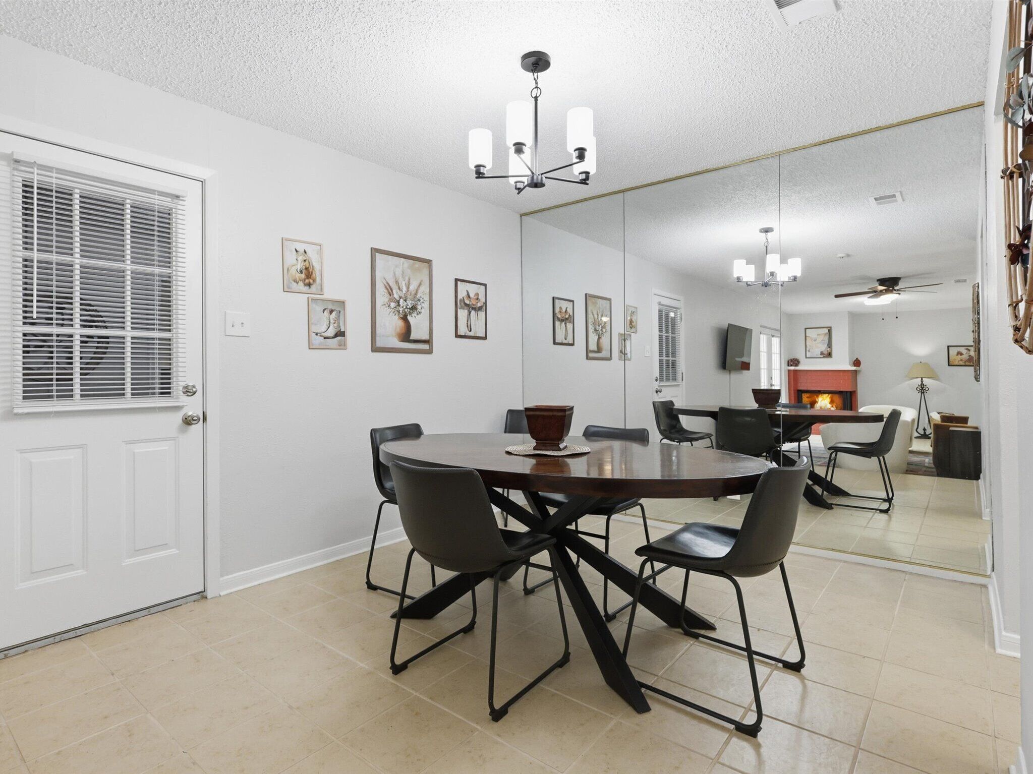 A dining area with a round table, black chairs, a chandelier, and framed artwork on the walls.