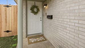 Une porte blanche ornée d’une guirlande, une boîte aux lettres et un paillasson décoré de fleurs.