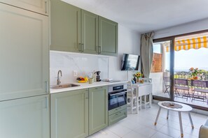 A modern kitchen with a built-in oven and a dining area with a small table and chairs. - ANGE GARDIEN VI AP4502 By Riviera Holiday Homes (Villefranche-sur-Mer)
