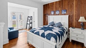 Un dormitorio con cama, mesita de noche, lámpara, cómoda, silla, escalera y puerta que da a un área exterior.
