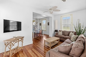 A living room with a TV, wooden furniture, a ceiling fan, and a large window. - Short walk to beach/close to attractions (Galveston)