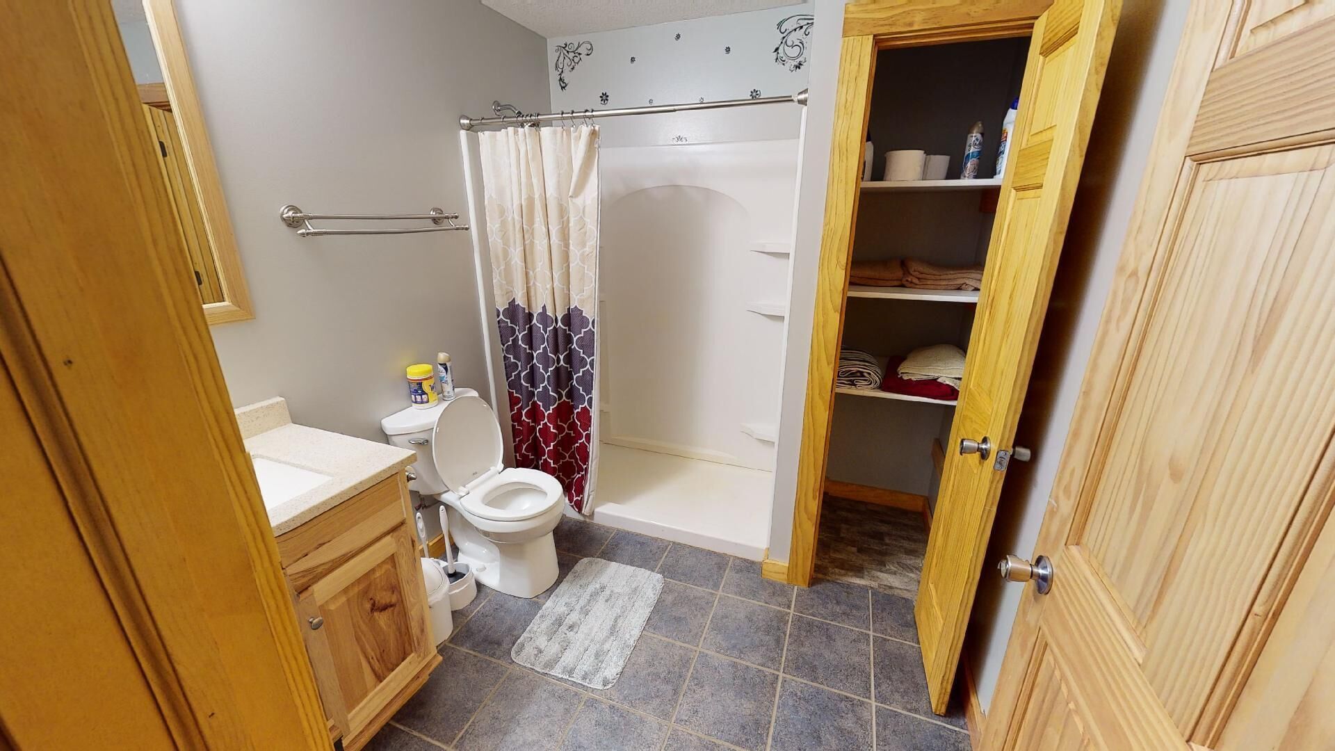 A bathroom with a toilet, shower, and wooden cabinets.