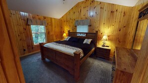 Camera da letto con rivestimento in legno, un letto, due lampade da comodino, un comodino e una finestra.