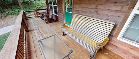 Una terraza de madera con una mesa de vidrio y bancos, una puerta verde y una ventana.