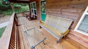 Eine Holzterrasse mit einem Glastisch und Bänken, einer grünen Tür und einem Fenster.