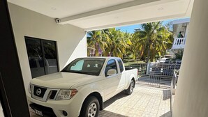 A white pickup truck parked inside a covered area with tiled flooring and a view of palm trees and a building in the background. - Surf City Beach House with Private Pool – 5-10 Min Walk to Beach, Near El Tunco (Playa San Blas)