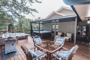 A covered outdoor deck with wicker furniture, a hot tub, and a grill. - Luxurious Retreat with Pool and Game Room (Logan)