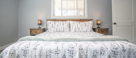 Un dormitorio con cama, dos mesitas de noche, una ventana con persianas y una puerta.
