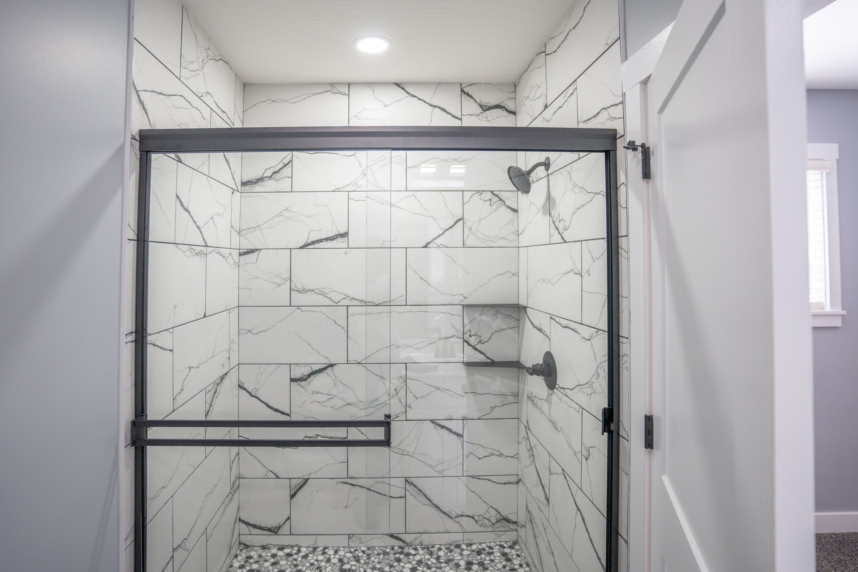 Une douche avec une porte en verre, des carreaux de marbre et un sol recouvert de petits galets.