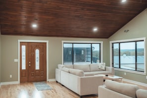 A spacious living room with a wooden ceiling, large windows, and a beige sofa. - Luxurious Retreat with Pool and Game Room (Logan)