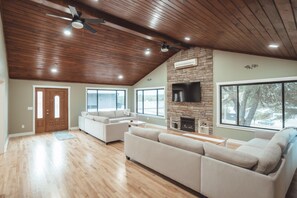 Un salón amplio con techo alto, vigas de madera, chimenea y ventanas grandes.