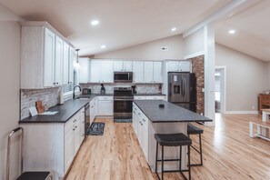 A modern kitchen with white cabinets, a central island, and a brick accent wall. - Luxurious Retreat with Pool and Game Room (Logan)