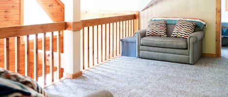 Una habitación con un sofá gris, una barandilla de madera y vistas a un balcón.