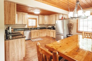 A kitchen with wooden cabinets, a stainless steel refrigerator, and a wooden dining table. - Scotts Creek Cabins - Hem Loch (Logan)