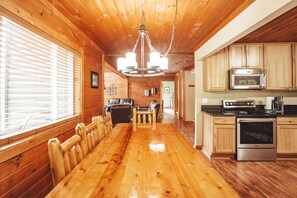 Un interior de madera con una larga mesa de comedor, armarios de madera y una zona de cocina con microondas y estufa.