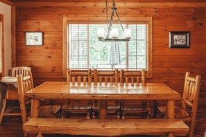 A wooden dining table with benches, a chandelier, and framed pictures on the walls. - Scotts Creek Cabins - Hem Loch (Logan)