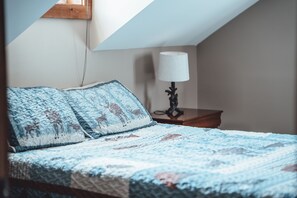 A bedroom with a bed, a nightstand, a lamp, and a window. - Scotts Creek Cabins - Hem Loch (Logan)
