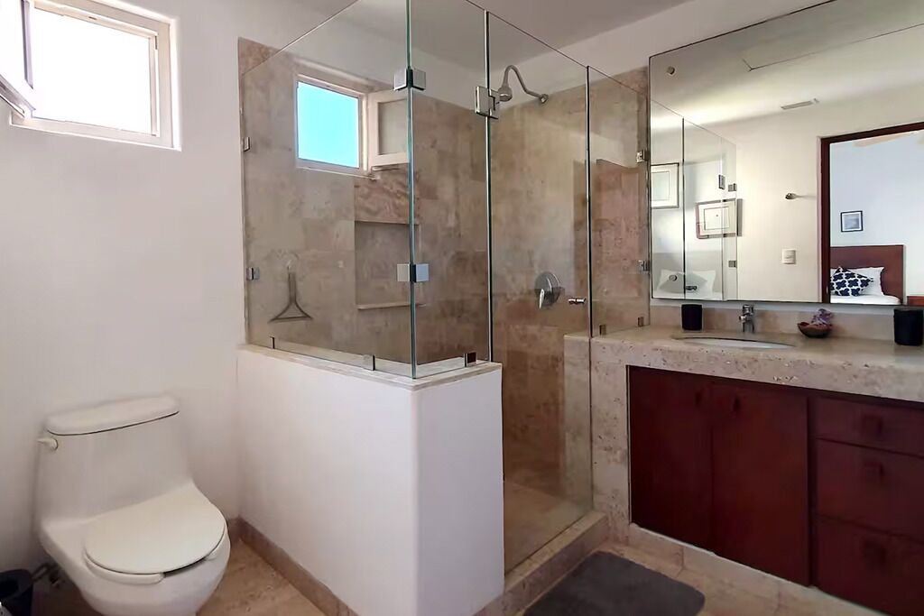 A bathroom with a glass-enclosed shower, a toilet, a vanity with a mirror, and a sink.