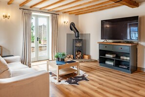 A living room with a sofa, a wooden coffee table, a TV, a fireplace, and a bookshelf. - The Cottage at Tuffon Hall, Sible Hedingham, Suffolk (Sible Hedingham)