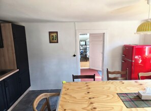 A dining area with a wooden table, chairs, a red refrigerator, and a door leading to another room.