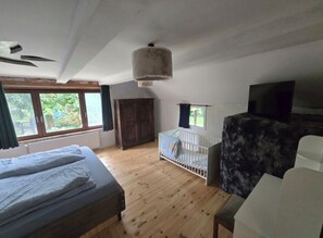 A room with a bed, a crib, a wardrobe, and a television.