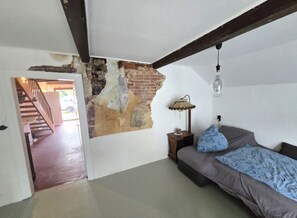 Una habitación con paredes de ladrillo visto, una escalera, una cama con colcha estampada, una lámpara de pie y un colgante de techo.
