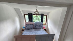 A bedroom with a single bed, a window with curtains, a small bedside table with a lamp, and a ceiling light fixture.