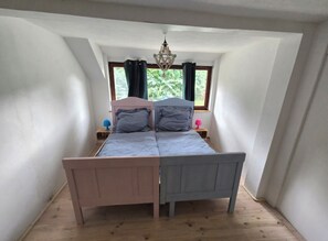 Un dormitorio con una cama individual, una ventana con cortinas, una mesita de noche pequeña con lámpara y una lámpara de techo.