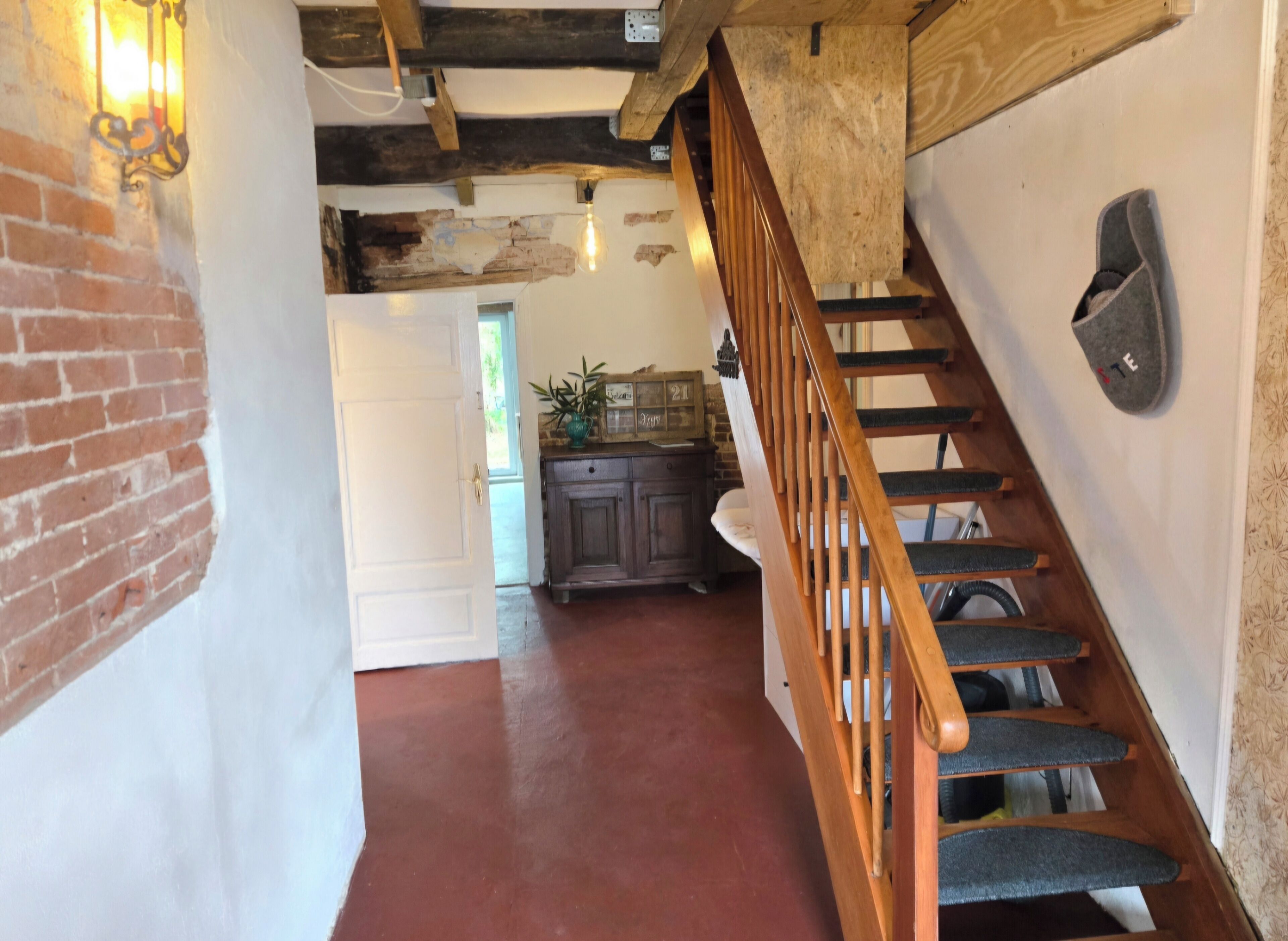 Un escalier avec des marches en bois et une rampe, menant à une pièce dotée d’une porte blanche et d’un mur en briques.