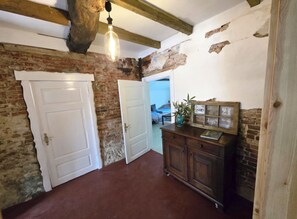 Una habitación con paredes de ladrillo visto, techo de madera, una puerta blanca y un mueble con marco envejecido.