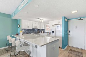 Une cuisine moderne dotée d’un grand îlot central, de meubles blancs, d’un mur d’accent bleu et d’une horloge au mur.
