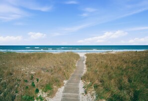 Un sentier côtier qui mène à la plage, avec des dunes de chaque côté.