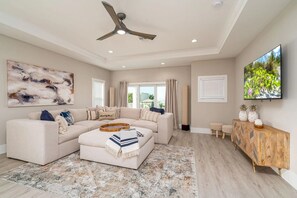 A living room with a sectional sofa, a ceiling fan, a flat-screen TV, and a large abstract painting. - Beach To Bay Vacation Home (Fort Myers Beach)