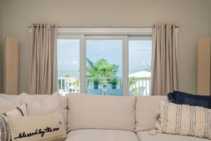 A room with a beige sofa, a view of the sea, and a balcony with plants. - Beach To Bay Vacation Home (Fort Myers Beach)