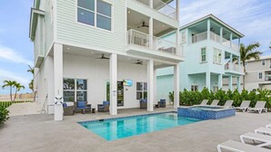 Ein zweistöckiges Gebäude mit Pool, Sitzgelegenheiten im Freien und Blick auf den Strand.