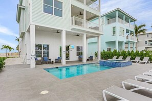 Ein zweistöckiges Gebäude mit Pool, Sitzgelegenheiten im Freien und Blick auf den Strand.