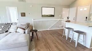 A modern living room with a white sofa, a small table, and a kitchen area with stools. - Good Vibes LKA Lakeview with Boat Slip (Orange)