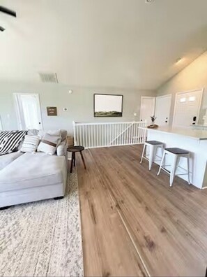 A modern living room with a white sofa, a small table, and a kitchen area with stools. - Good Vibes LKA Lakeview with Boat Slip (Orange)