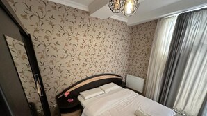 A bedroom with a bed, a nightstand, a dresser, a radiator, and a window with curtains.