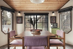 A dining area with a wooden table, purple chairs, a vase with branches, and framed pictures on the walls. - Whispering Pines | EV Chrg, Near Trails, Dogs Ok! (Big Bear)