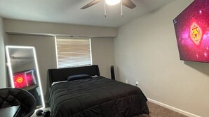 Un dormitorio con una cama, un ventilador de techo, un televisor de pared y una ventana con persianas.