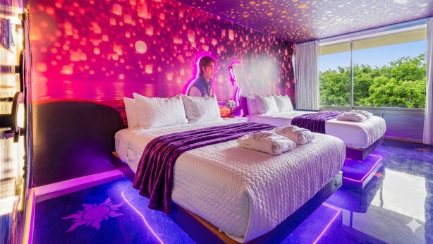 A modern hotel room with a large bed, a separate seating area, and a view of greenery outside. - Rapunzel themed studio w/ pool & workspace (Kissimmee)